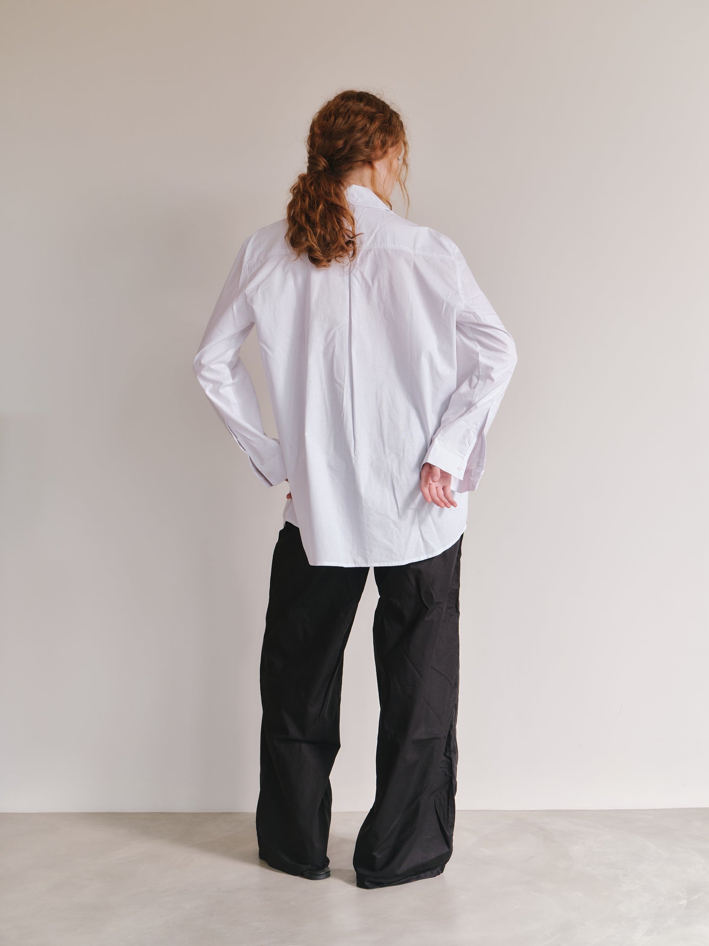 Person wearing a white shirt and black pants against a plain background