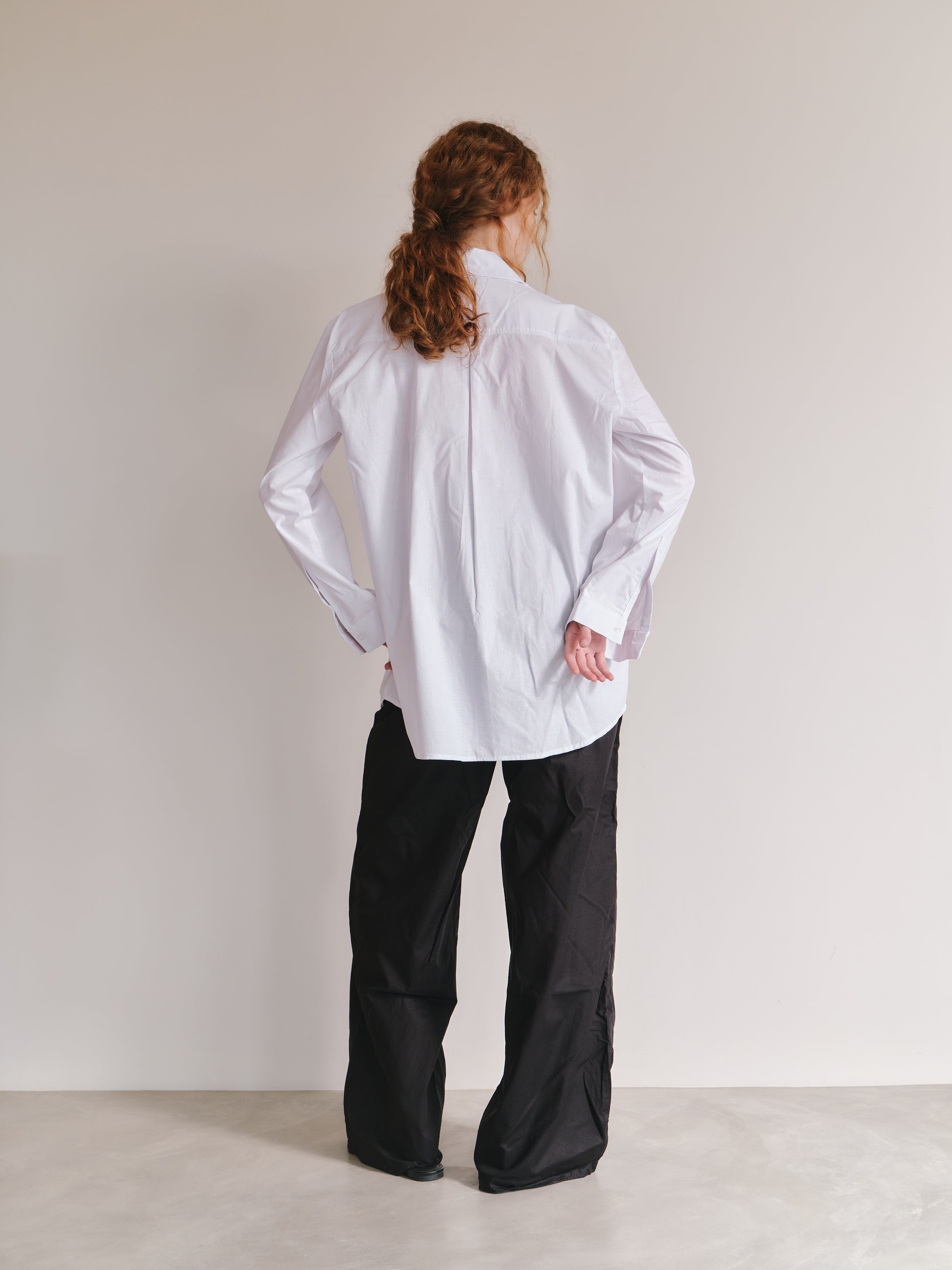 Person wearing a white shirt and black pants against a plain background
