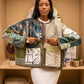 A woman stands in a warm indoor setting wearing a patchwork quilted jacket with mixed botanical and geometric patterns in beige, green, blue, and brown tones. The text 'Pause & Reflect' appears at the top of the image.
